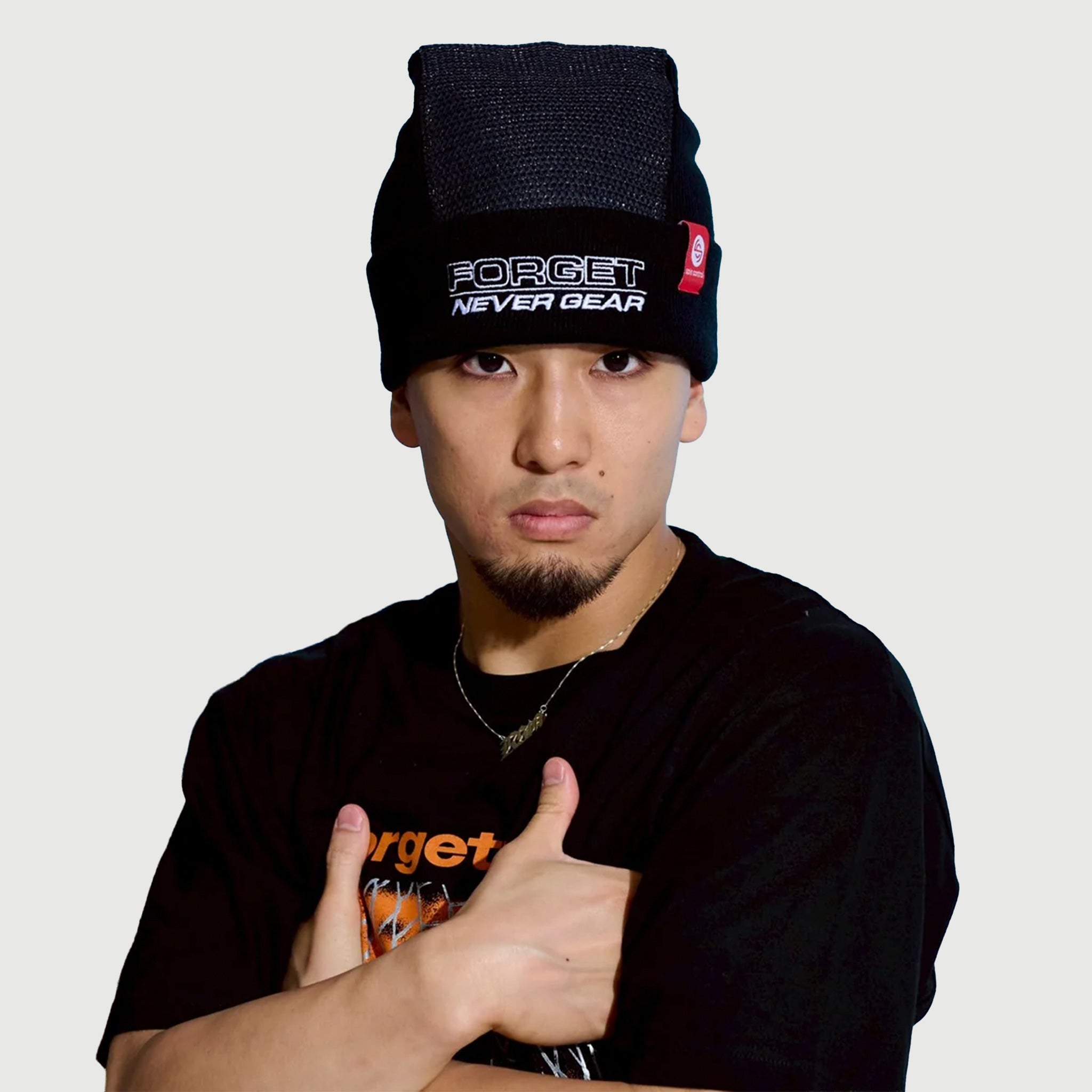Person wearing a black Spin Control Premium Spin Cap beanie with 'FORGET NEVER GEAR' text, with their arms crossed in front of a blue textured wall.
