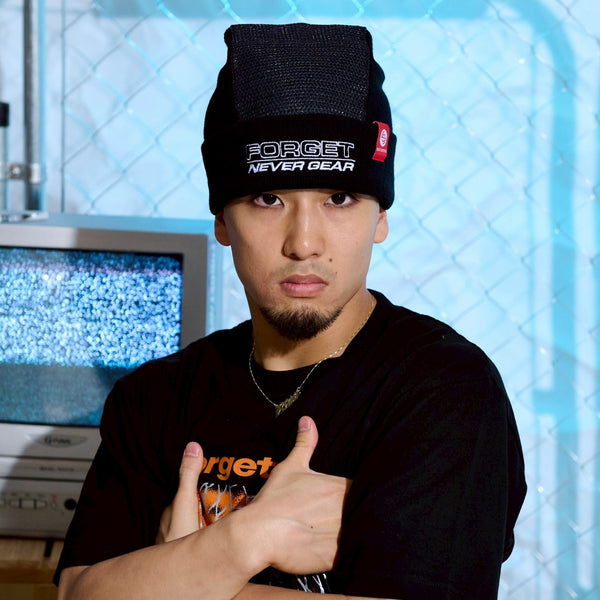 Person wearing a black Spin Control Premium Spin Cap beanie with 'FORGET NEVER GEAR' text, with their arms crossed in front of a blue textured wall.