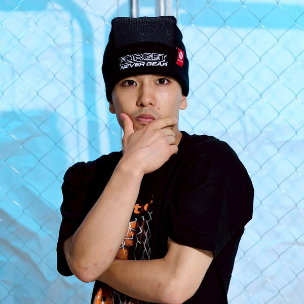 Bboy Ryo-Spin wearing a black Spin Control Premium Sin Cap beanie and black t-shirt with a graphic design, posing against a light blue textured background.
